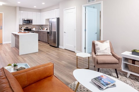 a living area with a couch chair coffee table and a kitchen in the background