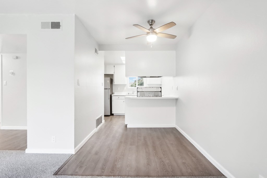 A room with a ceiling fan and a kitchen island in the background.