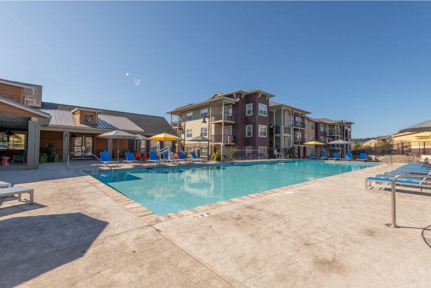a swimming pool with chaise lounge chairs and umbrellas in front of a building