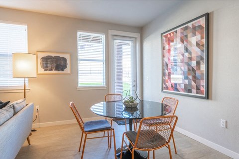 Apartments for Rent in Tigard - Sygnii - Dining Area with Round Glass-Top Dining Table, Four Metal-Framed Chairs, and Floor Lamp.