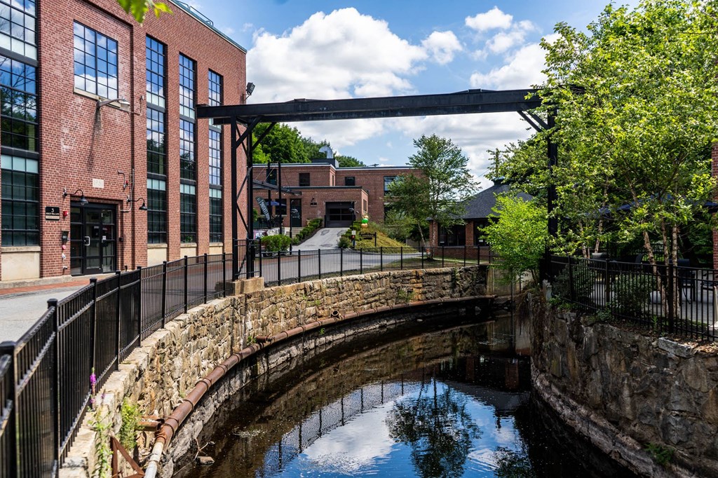 Brick buildings along a canal with stone walls and a metal overhead beam.