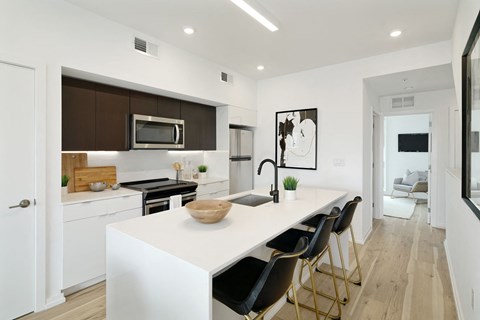 A modern kitchen with white countertops and black chairs.
