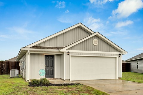 A house with a grey garage door and a sign on the lawn.
