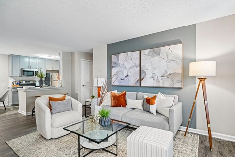 A living room with a grey sofa, a glass coffee table, and a large abstract painting on the wall.