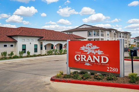 The Grand at Oak Grove is a white building with a red sign in front.