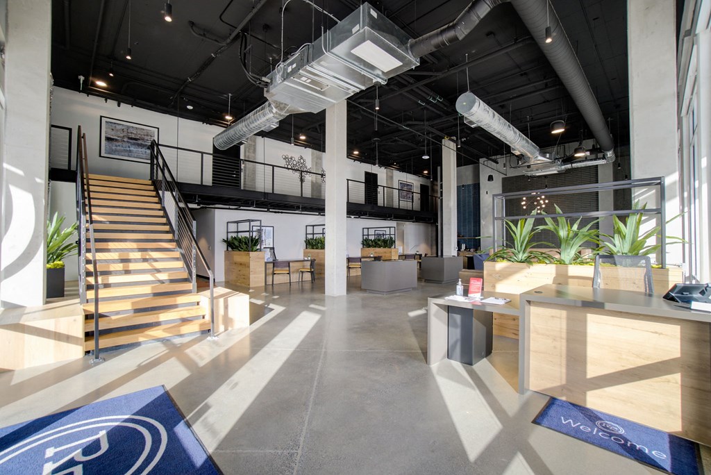 the lobby of a building with stairs and tables and plants