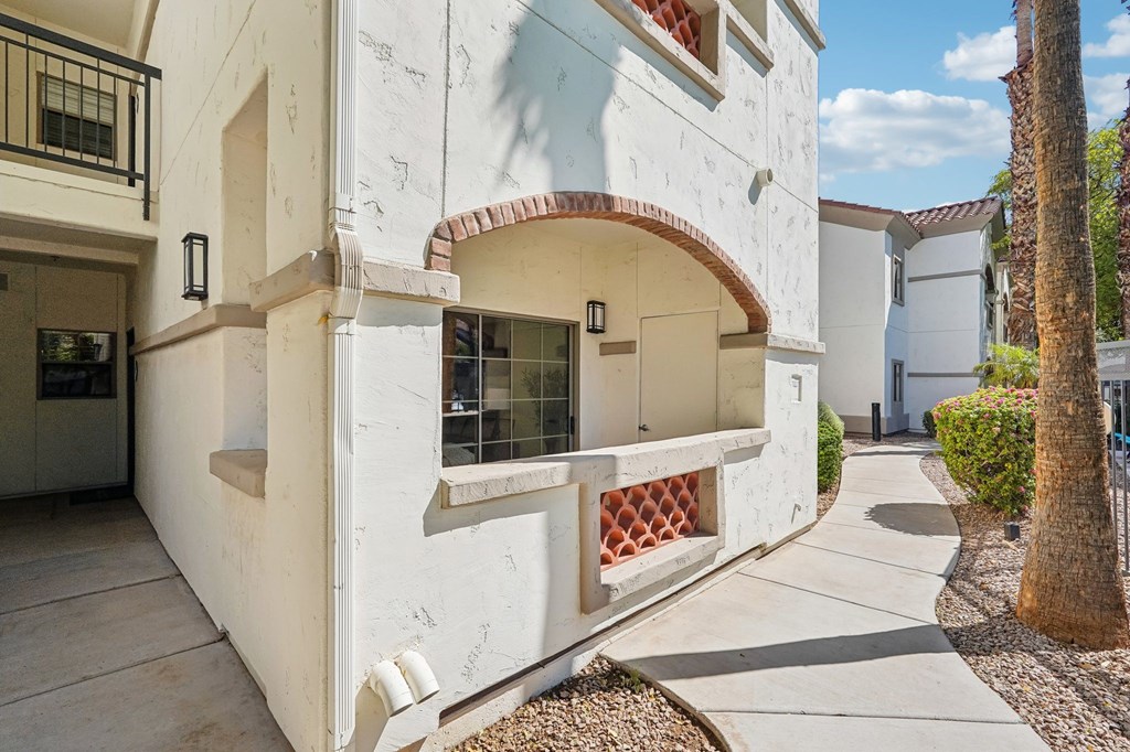 A white building with a red tile roof and a balcony with a lattice design.
