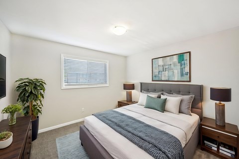Modern bedroom with gray upholstered bed, blue accents, and abstract art.