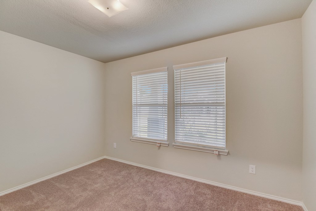 an empty bedroom with two windows and carpeting