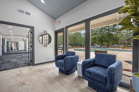 Two blue chairs are placed in a room with a view of a pool and trees outside.