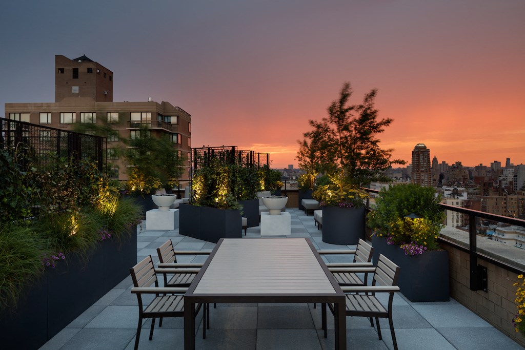 a rooftop terrace with a table and chairs and a city skyline at sunset