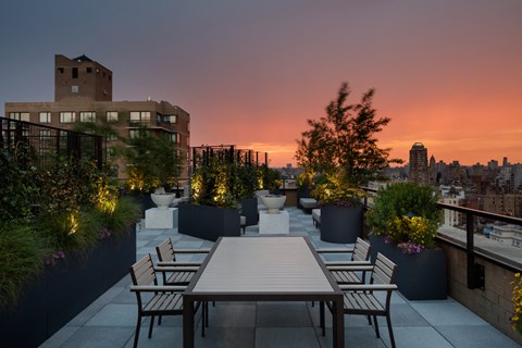 a rooftop terrace with a table and chairs and a city skyline at sunset