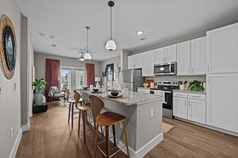 A kitchen with white cabinets and a large island with chairs around it.