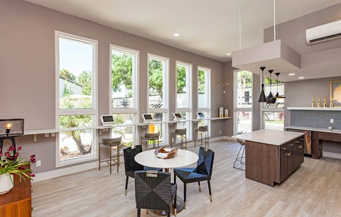 A modern kitchen with a dining table and chairs in the foreground and a balcony with a view of trees and a house in the background.