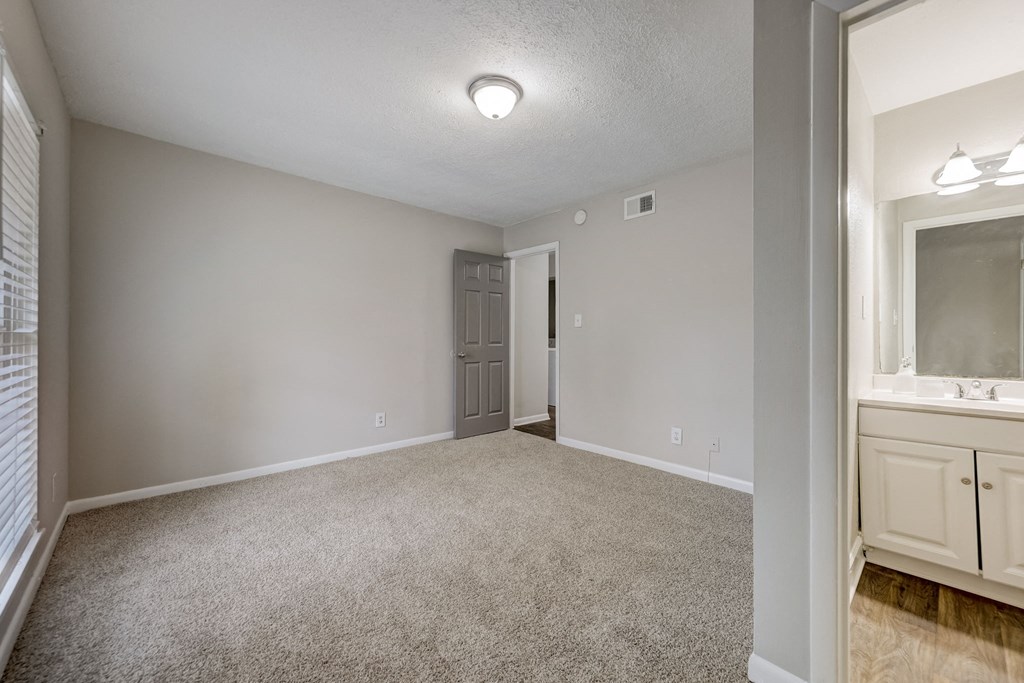 Pet-Friendly Apartments in Sandy Springs – Celebration at Sandy Springs - an empty living room with white carpet and a door to a bathroom