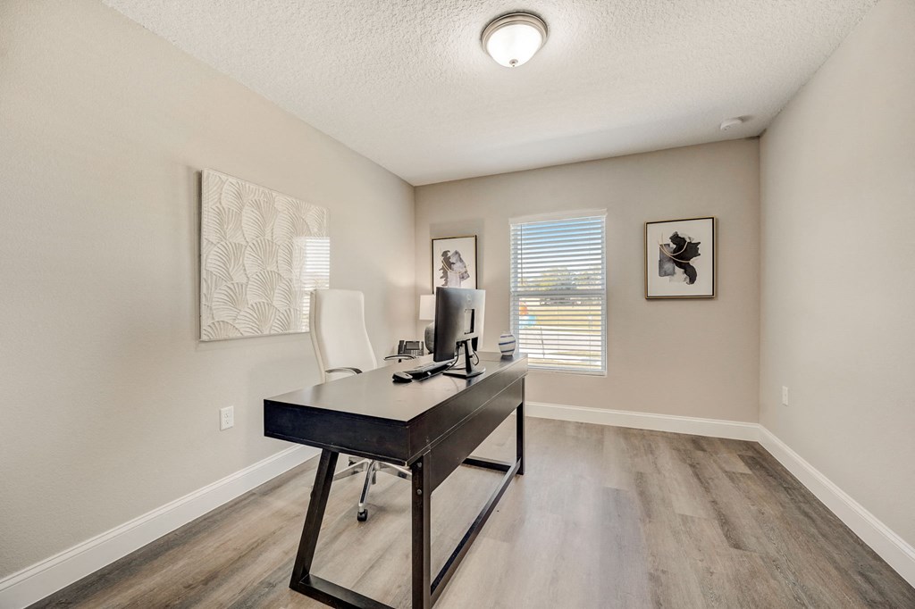 Spacious office area with a desk, chair, and large window at The Groves at Lake Ella in Lady Lake, Florida, a pet-friendly rental community.