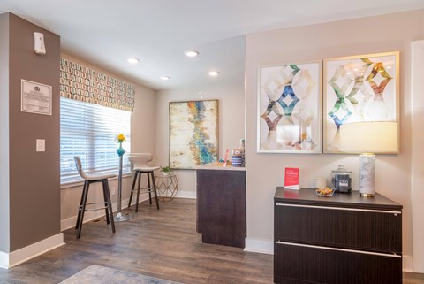 a living room with a bar and a dining room with chairs and paintings