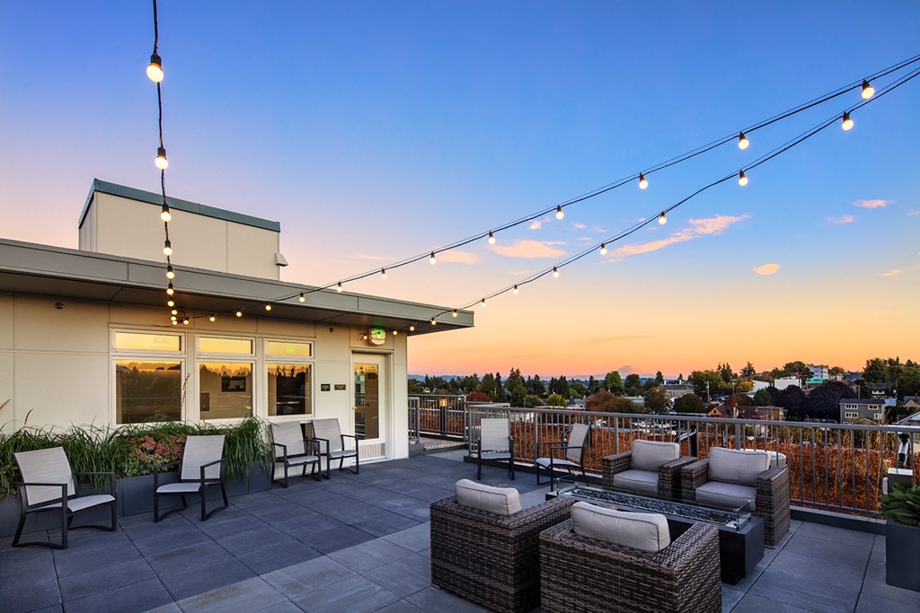 Apartments in Greenwood - The Morrow Rooftop Deck with Comfy Seating, Hanging Lights, Rectangular Fire Feature, and a Panoramic View of the City