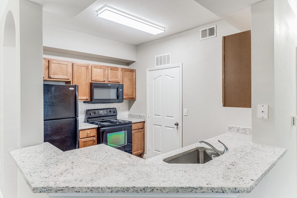 One-Bedroom Apartments in San Antonio, TX - Club at Stone Oak - Kitchen with Granite Countertops, Wood-Style Cabinets, and Black Appliances
