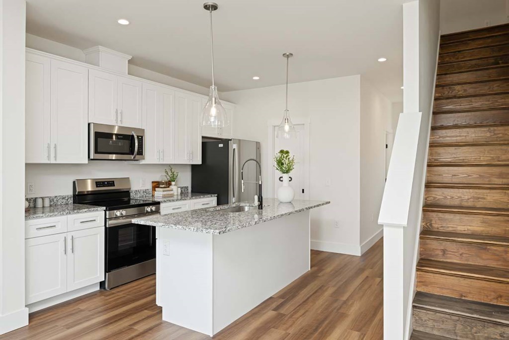 A modern kitchen with white cabinets and a wooden staircase.