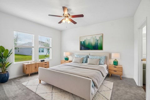 A bedroom with a large bed, a ceiling fan, and a painting on the wall.
