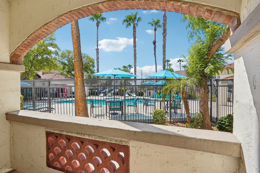 A view from a window looking out at a pool surrounded by palm trees.