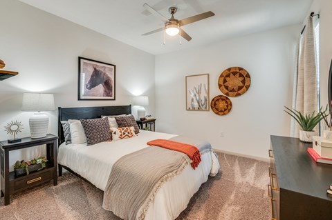 Three-Bedroom Luxury Apartments in Waco, TX - 2201 Creekview - Bedroom With Ceiling Fan, Plush Carpet, Neutral Bedding, Dark Wood Furniture, Large Window, And Decorative Wall Art.