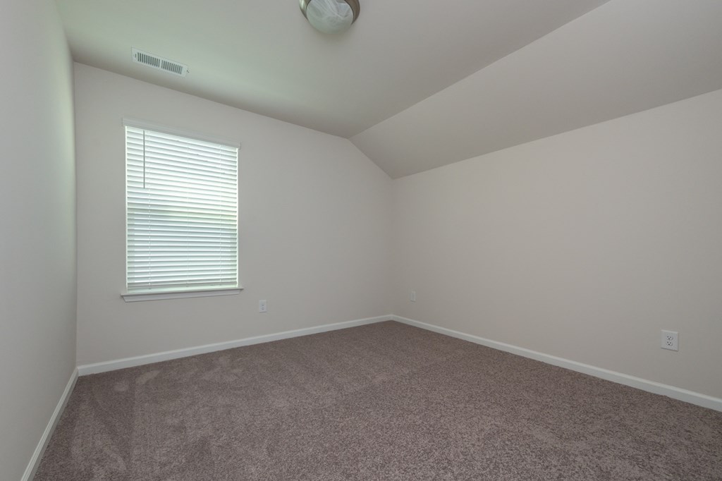 a bedroom with a carpeted floor and a window with a blind