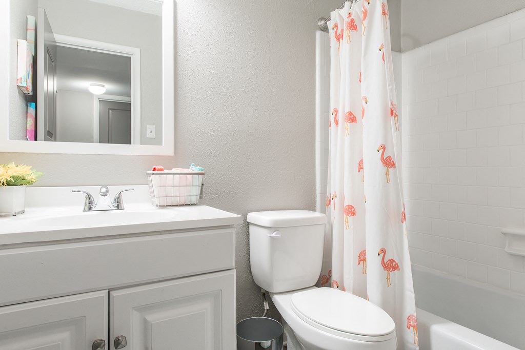 Sandy Springs, GA Apartments – Celebration at Sandy Springs -  a bathroom with a white sink and toilet next to a bathtub with a shower curtain