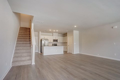 an empty living room with a kitchen and stairs