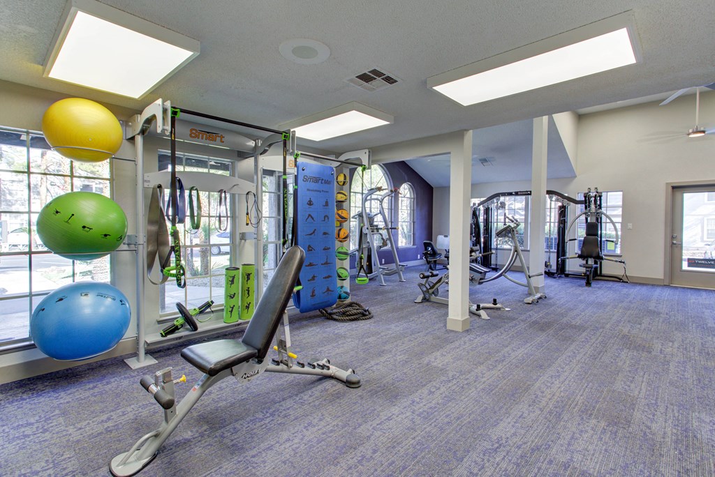a gym with cardio equipment and weights in a building with windows