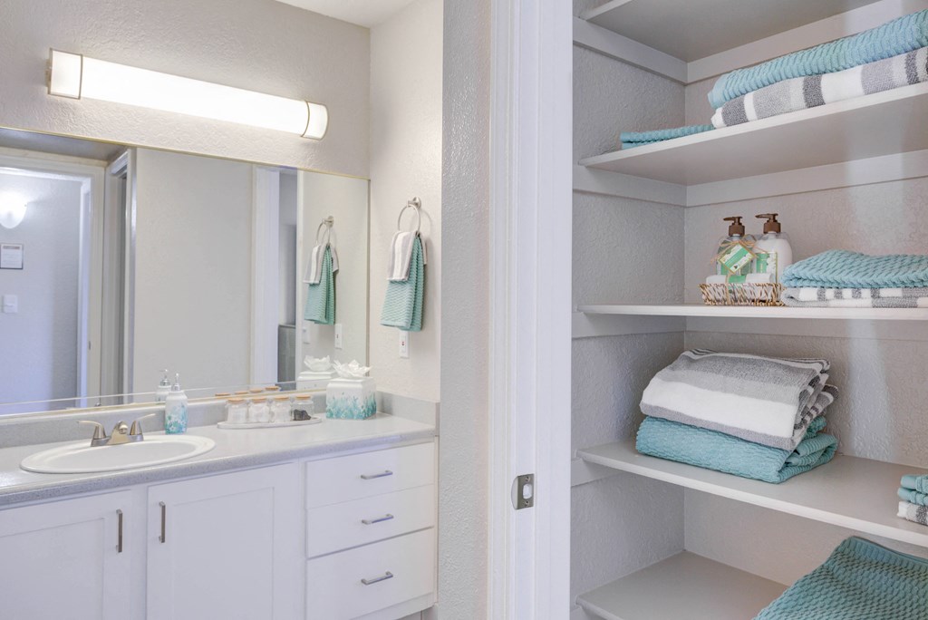 a bathroom with a sink and a mirror and shelves with towels