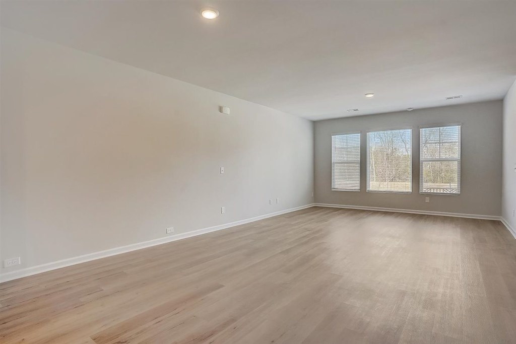 A spacious room with wooden flooring and a window with blinds.