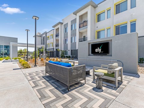 A modern outdoor seating area with a bench, table, and chairs in front of a building with a large Ely sign.