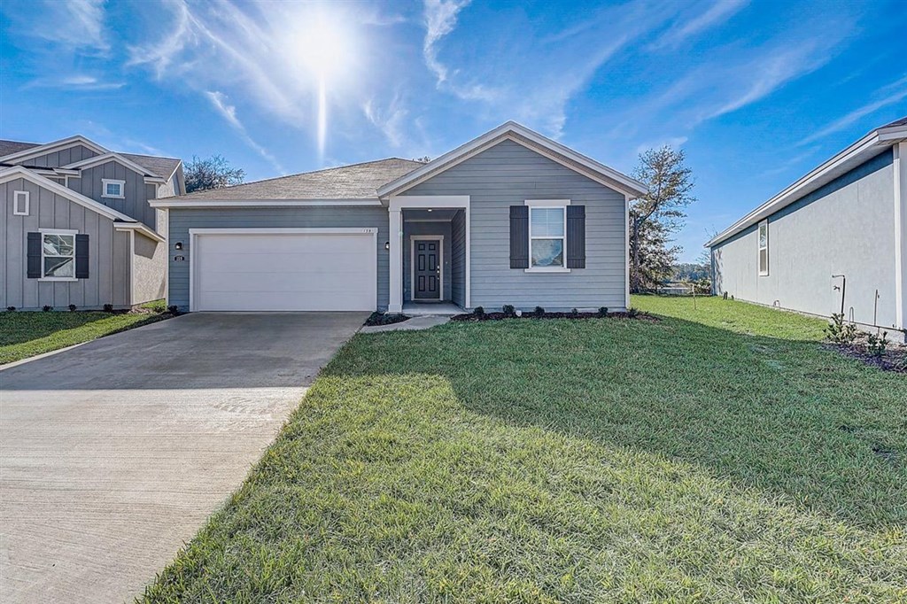 Exterior view of a single-story, light blue house with a white garage door and dark shutters.