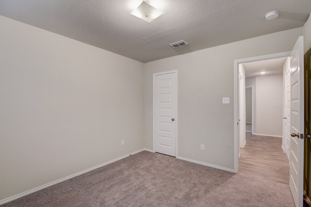 an empty room with a hallway and a door to a bedroom