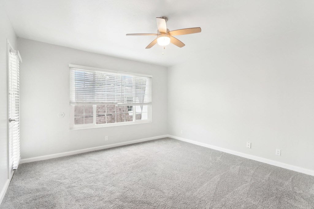 A room with a ceiling fan and a window with blinds.