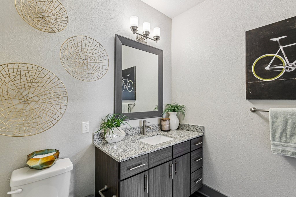 A bathroom with a white toilet, a sink with a mirror above it, and a bicycle drawing on the wall.