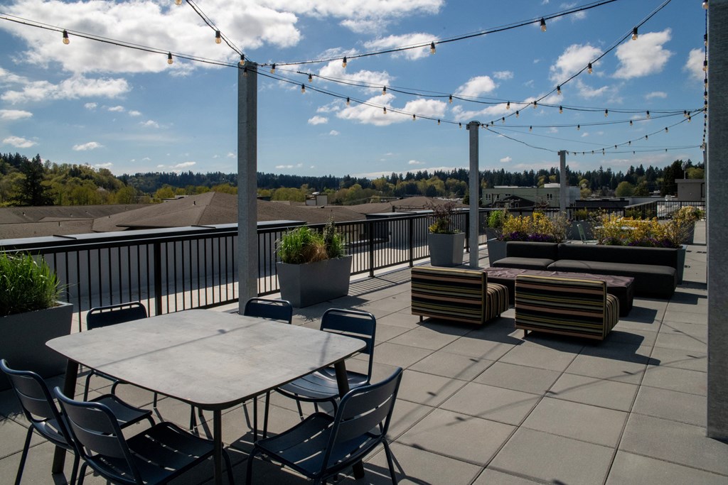 Bothell, WA, Apartments Near UW Bothell - Morado Bothell - Rooftop Deck with Outdoor Seating, Dining Area, String Lights, and Plant Boxes.