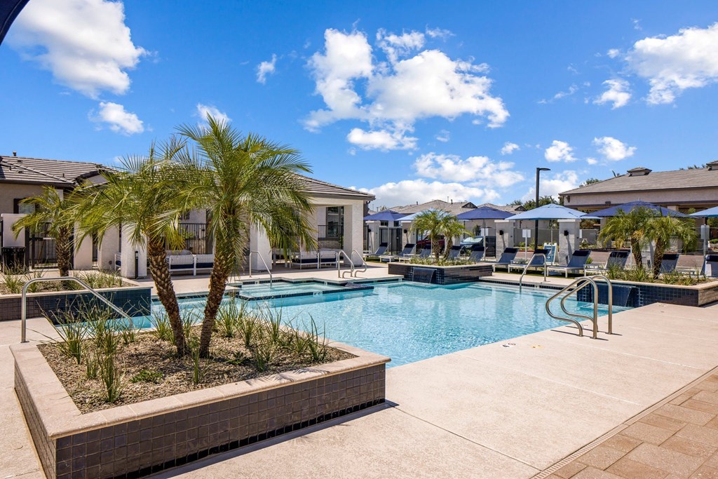 Phoenix AZ Apartments - The Crofton at Sheely Farms - Large Pool with a Hot Tub, Fountains, Plant Beds, Poolside Lounge Chairs, and Umbrellas, Shot at Sunset