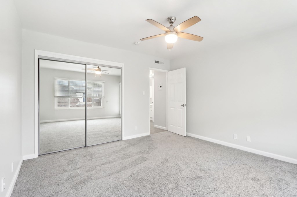 Pet-Friendly Apartments In Fremont, CA - Brookvale Chateau - Spacious Bedroom With Plush Carpeting, Sliding Mirror Closet Doors, Large Window, And A Ceiling Fan
