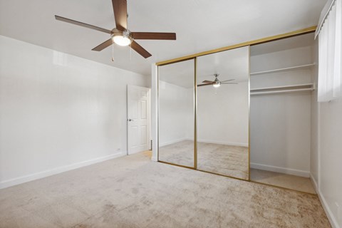 2-Bedroom Apartments in San Lorenzo, CA - Lorenzo Commons - Bright Bedroom With Carpet Flooring, Ceiling Fan, Mirrored Closet Doors, White Walls, And Window With Vertical Blinds.