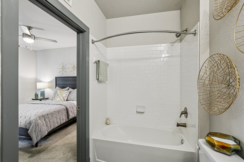 A bathroom with a white tub and a bedroom with a bed and a ceiling fan.