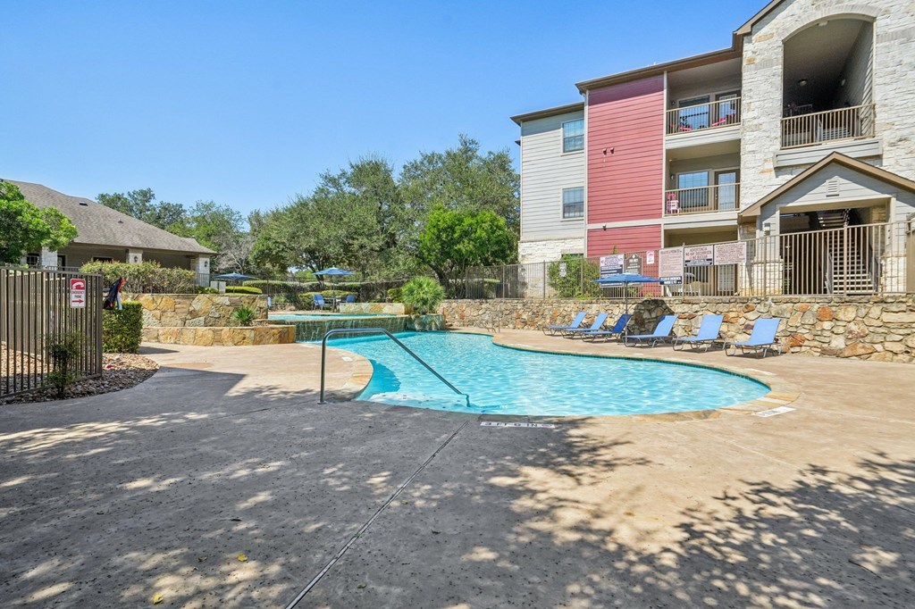 A swimming pool surrounded by a stone wall and chairs.