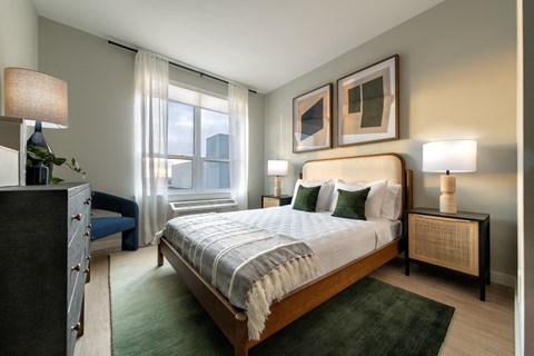 A bedroom with a large bed, a nightstand, and a window with curtains.