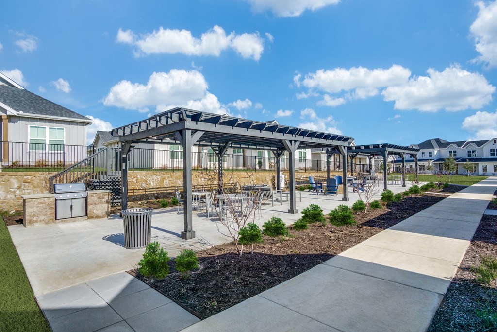 A sunny day at a park with a walkway, benches, and a canopy.