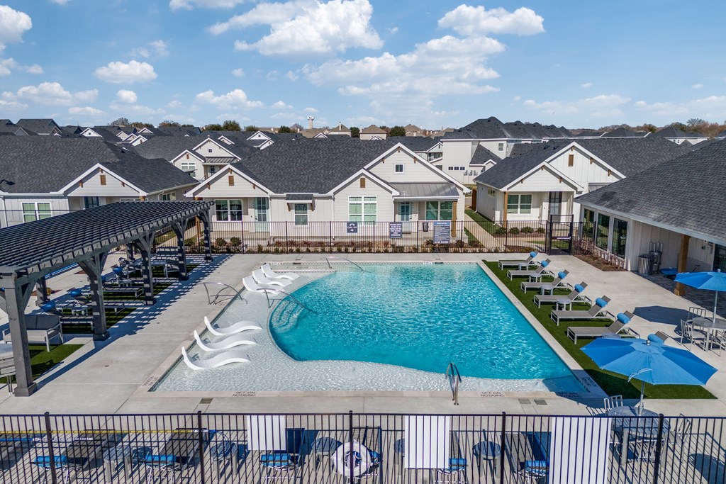 A large swimming pool surrounded by lounge chairs and umbrellas in a residential area.