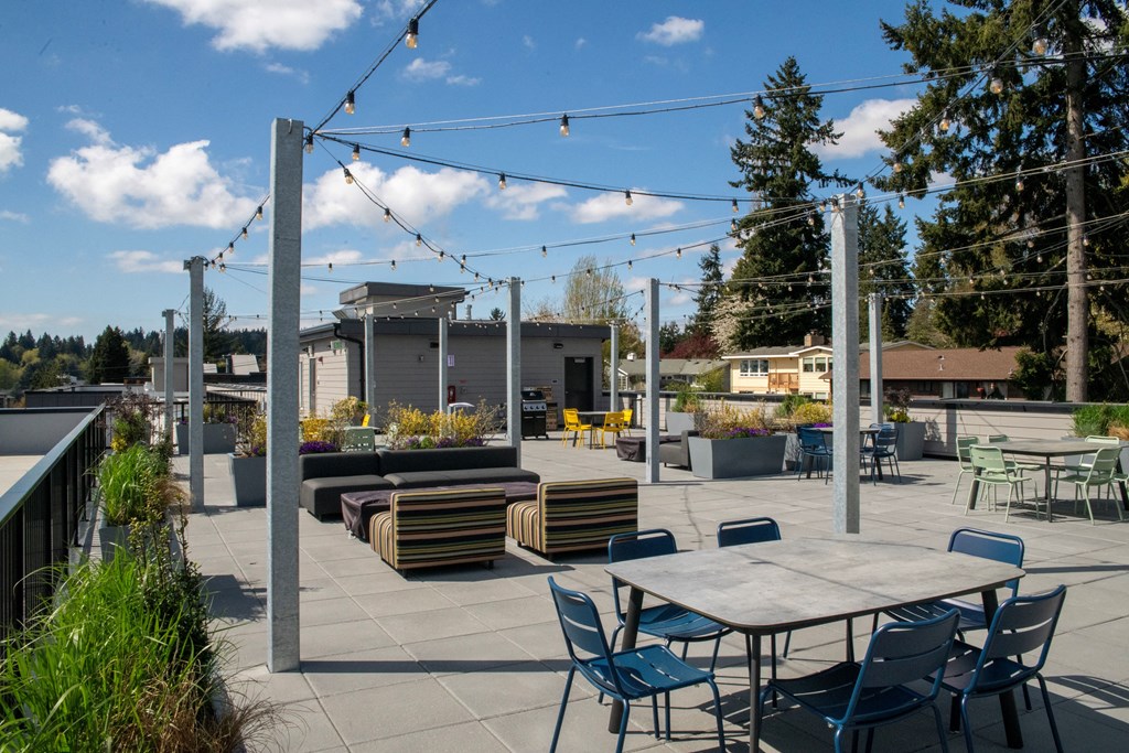 Apartments Near UW Bothell In Bothell, WA - Morado Bothell - Rooftop Deck Overlooking Stunning Nature Views With BBQs, Firepits, Outdoor Seating, Tables, And Outdoor String Lights.