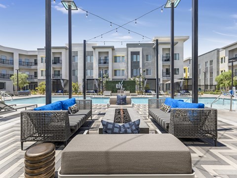 A pool area with lounge chairs and a pool in front of apartment buildings.
