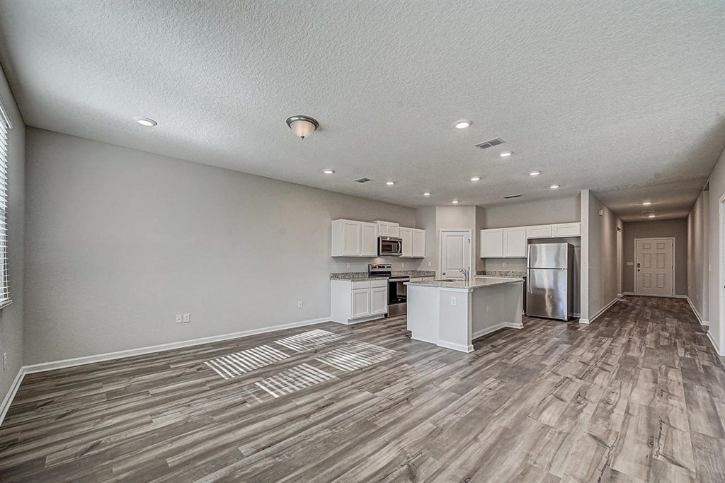 Open-concept living space with gray wood floors, white kitchen cabinets, and stainless steel appliances.
